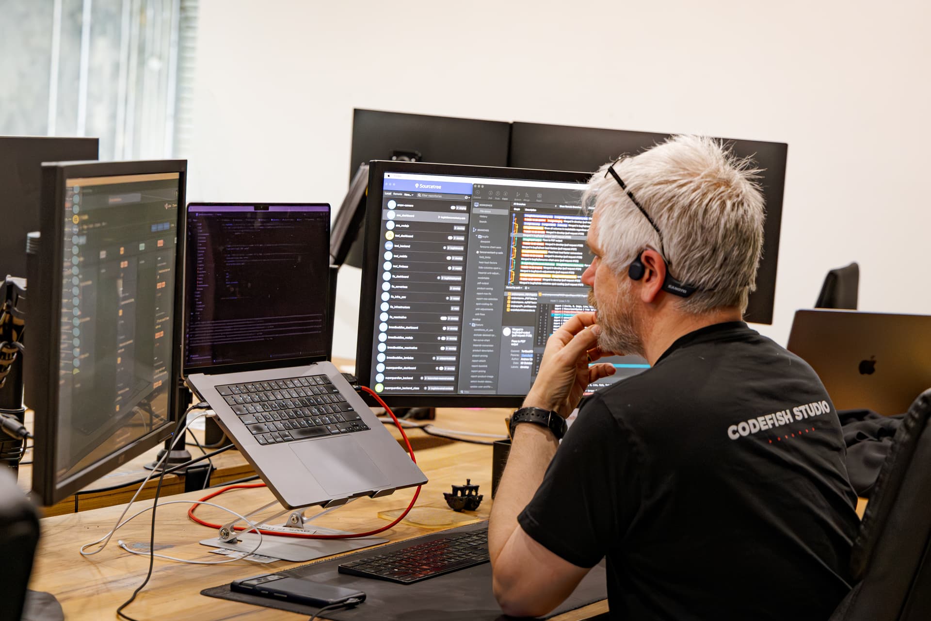 A CodeFish developer working across three monitors, reviewing code and version history