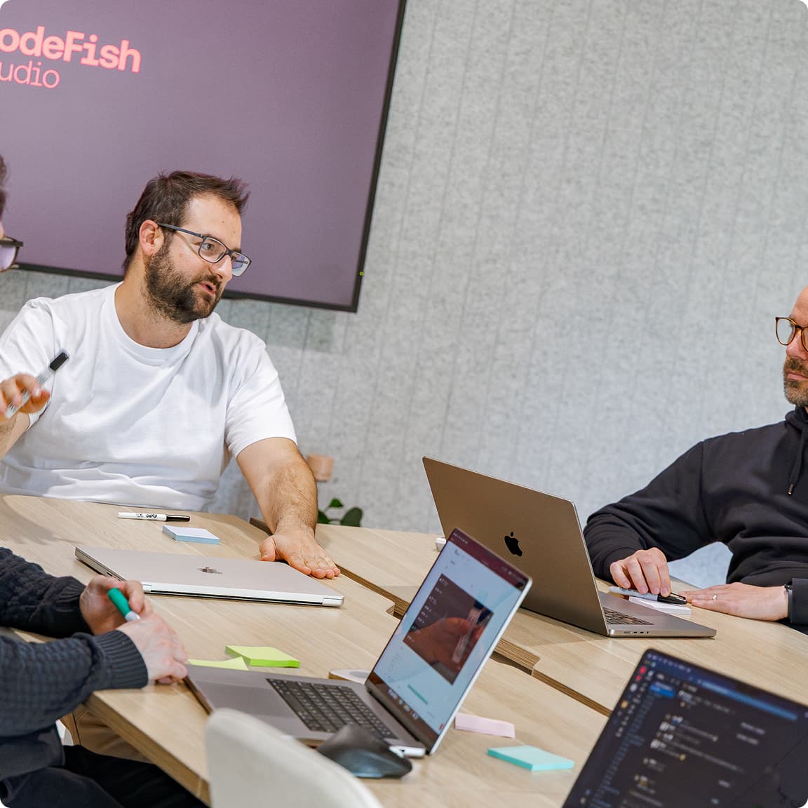Four CodeFish team members working through a problem around a table of laptops, CodeFish Studio sign on the wall